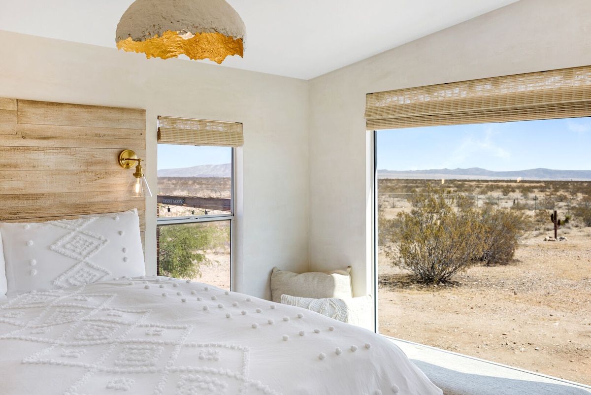 Ein Schlafzimmer mit einem großen Bett, einem Holz-Kopfstück, einer Pendelleuchte und Blick auf eine Wüstenlandschaft durch ein Fenster.