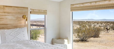 Un dormitorio con una cama grande, cabecera de madera, lámpara colgante y vistas a un paisaje desértico a través de una ventana.