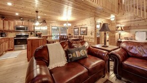 A cozy log cabin interior with a dining area, kitchen, and a leather couch with a throw blanket. - Toccoa River Fun + Hot Tub, Game Rm, Fish, Swim (Blue Ridge)