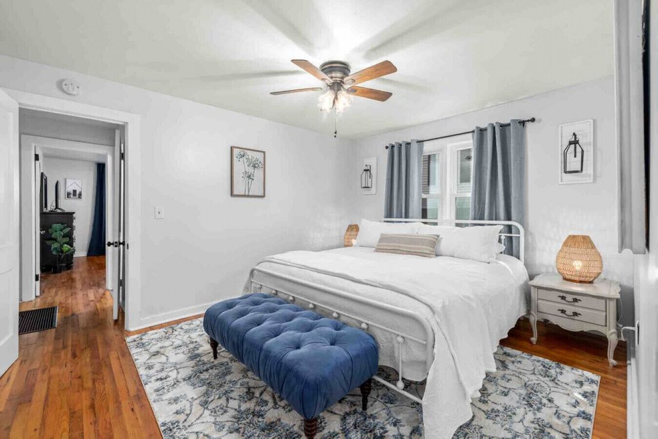 Quarto com cama, ventilador de teto, mesa de cabeceira, luminária e janela com cortinas.