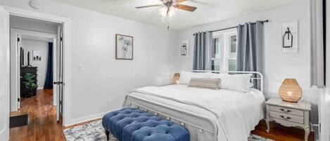 Quarto com cama, ventilador de teto, mesa de cabeceira, luminária e janela com cortinas.