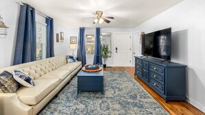 A living room with a beige sofa, a dark blue coffee table, and a TV on a blue cabinet.
