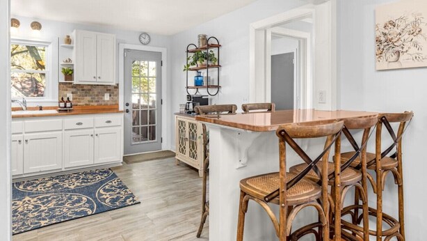A kitchen with white cabinets, a wooden countertop, and a dining area with wicker chairs.