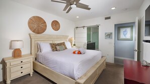 A bedroom with a bed, nightstand, lamp, ceiling fan, and artwork on the wall. - Steps to the Sand | Modern Oceanfront Condo, A/C, Dog-Friendly, Walk to Pier (Oceanside)