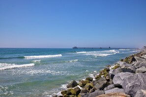 Uma costa rochosa com ondas quebrando nas pedras e um cais se estendendo para a água.