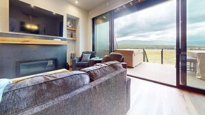 A modern living room with a fireplace, comfortable seating, and a large sliding glass door leading to a deck with a scenic mountain view.