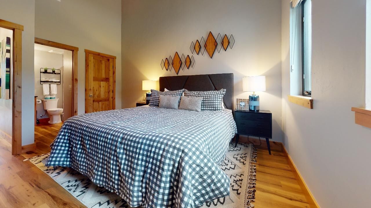 A bedroom with a large bed, a nightstand, a wall-mounted lamp, and a window.