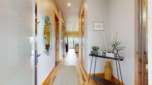 A hotel hallway with a wooden floor, a glass door, a mirror, a sign, and a small table with decorative items.