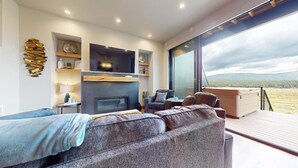 A modern living room with a fireplace, a sofa, and a view of a mountainous landscape through large windows.