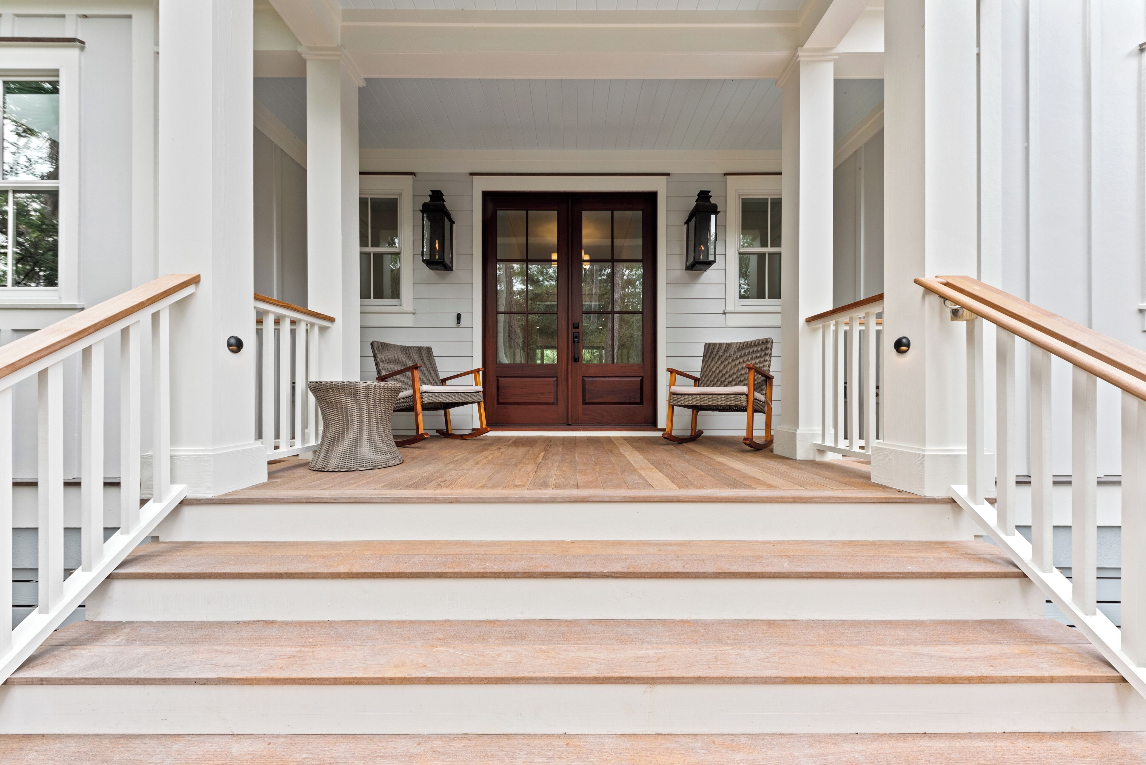 A front porch with a wooden staircase, white railings, and two wicker chairs.
