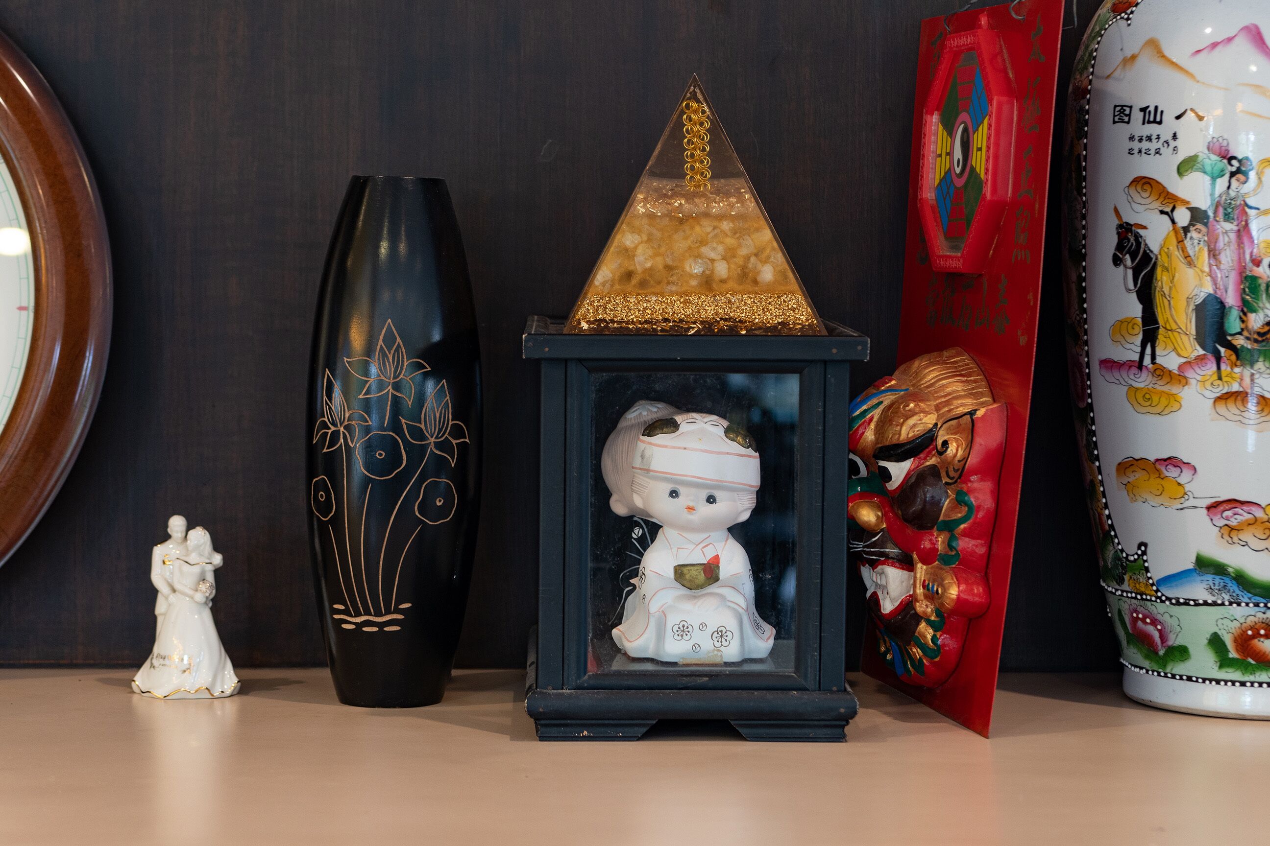 A display of various decorative items including a black vase with gold designs, a small white figurine, a framed glass object with a gold pyramid, a red decorative piece, and a white ceramic pot with colorful illustrations.