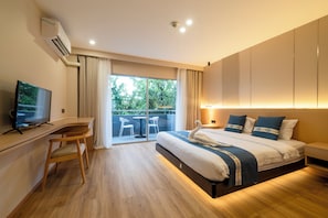 Ein modernes Hotelzimmer mit einem großen Bett, einem Schreibtisch, einem Fernseher und einem Balkon mit Blick auf Grünflächen.