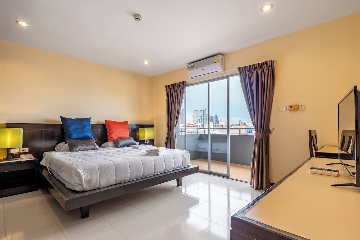 Une chambre d’hôtel moderne dotée d’un grand lit, d’un bureau et offrant une vue sur le paysage urbain grâce à de grandes fenêtres du sol au plafond.