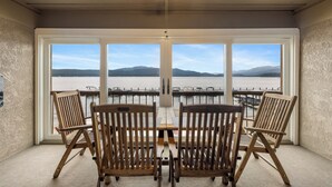 A balcony with a view of the water and mountains, wooden chairs, and a ceiling fan. - Lake Time - Crystal Beach - Lakefront - Beach - Seasonal Pool (McCall)