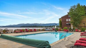 A pool area with red lounge chairs, a covered pool, and a view of mountains and a lake. - Lake Time - Crystal Beach - Lakefront - Beach - Seasonal Pool (McCall)