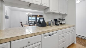 A modern kitchen with white cabinetry, a tiled countertop, and a dishwasher. - Lake Time - Crystal Beach - Lakefront - Beach - Seasonal Pool (McCall)