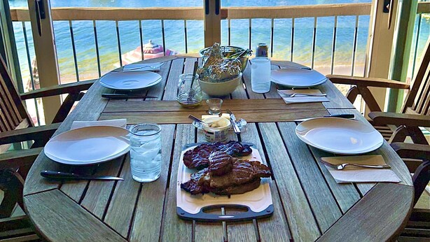 A wooden table set for two with plates, cutlery, and a glass of water. - Lake Time - Crystal Beach - Lakefront - Beach - Seasonal Pool (McCall)