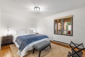A bedroom with a bed, bedside tables, a bench, a window with a view, and a ceiling light.