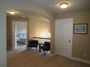 A hallway with a carpeted floor, a door, a bed in the adjacent room, and two chairs. - Masters Housing -5.6 miles to Masters (Martinez)