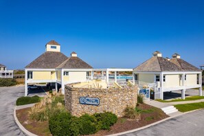 A beach club with a stone wall sign, covered structures, and a clear blue sky.