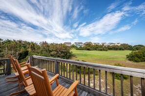 Une terrasse en bois, agrémentée de chaises, qui offre une vue sur un terrain de golf et des immeubles résidentiels.