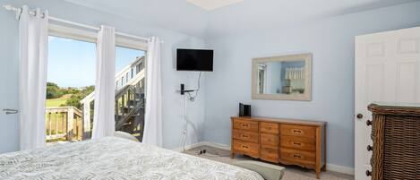 A bedroom with a bed, a dresser, a television, and a door leading to a balcony.