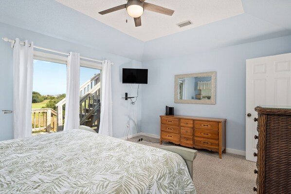 Une chambre à coucher comprenant un lit, une commode, un téléviseur et une porte donnant sur un balcon.