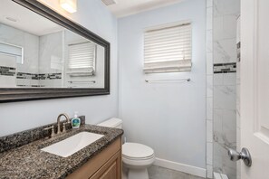 A bathroom with a granite countertop sink, a toilet, a shower with a glass door, and a mirror with a wooden frame.
