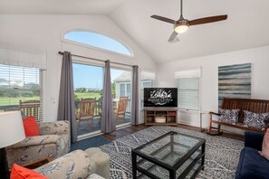 A spacious living room with a large TV, comfortable seating, and a view of the outdoors.