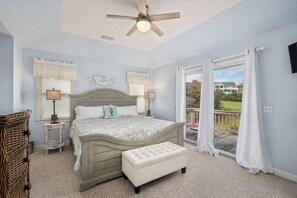 A bedroom with a bed, two bedside tables, a bench, a ceiling fan, and a view through a large window.