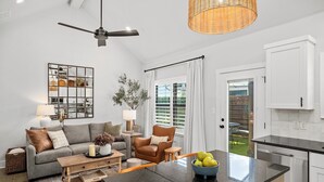 A modern living room with a sofa, coffee table, and a dining area with a kitchen in the background.