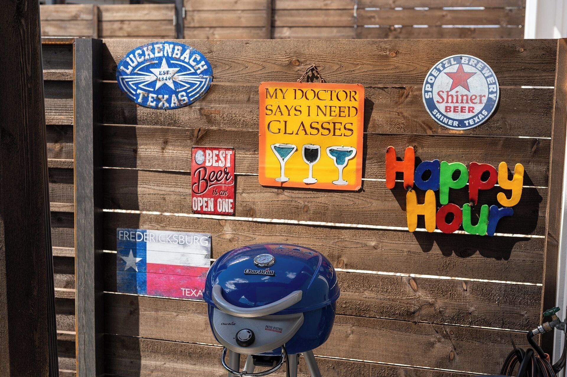 A wooden fence with various signs, including a Texas flag, a sign for Shiner Beer, and a sign that says "My doctor says I need glasses."