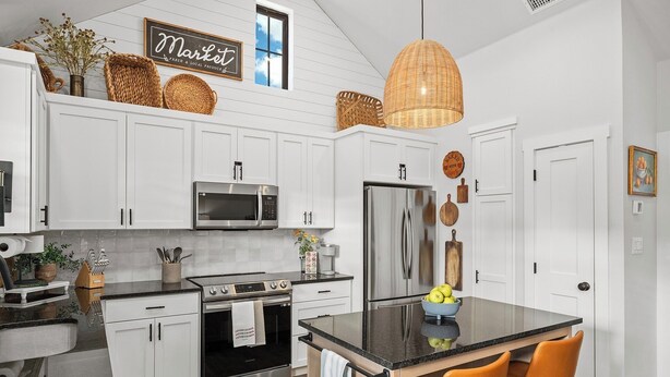 A modern kitchen with white cabinets, stainless steel appliances, a central island with chairs, and a hanging light fixture.