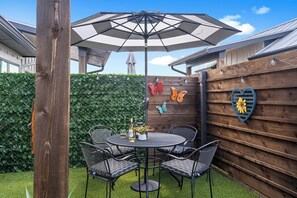 Un patio al aire libre con una mesa redonda y sillas, un paraguas grande y decoración de mariposas y corazones en la pared.