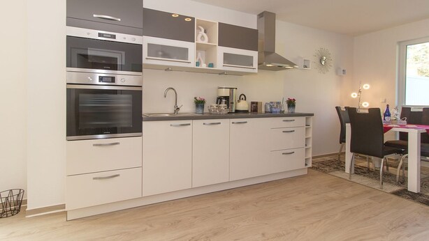 A modern kitchen with built-in appliances, a dining area with chairs, and a window providing natural light.