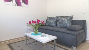 A modern living room with a grey sofa, patterned cushions, a white coffee table with a vase of pink flowers, and a painting of flowers on the wall.
