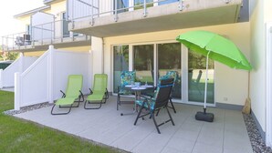 A patio with outdoor furniture, a green umbrella, and a view of a building with a balcony.