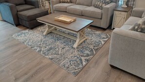 A living room with a grey sofa, a matching armchair, a coffee table, and a patterned rug.