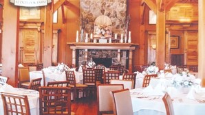 A dining area with wooden tables and chairs, a stone fireplace, and a chandelier.