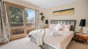 Un dormitorio con una cama grande, una mesita de noche, una ventana con cortinas, una lámpara de pared y un cuadro.