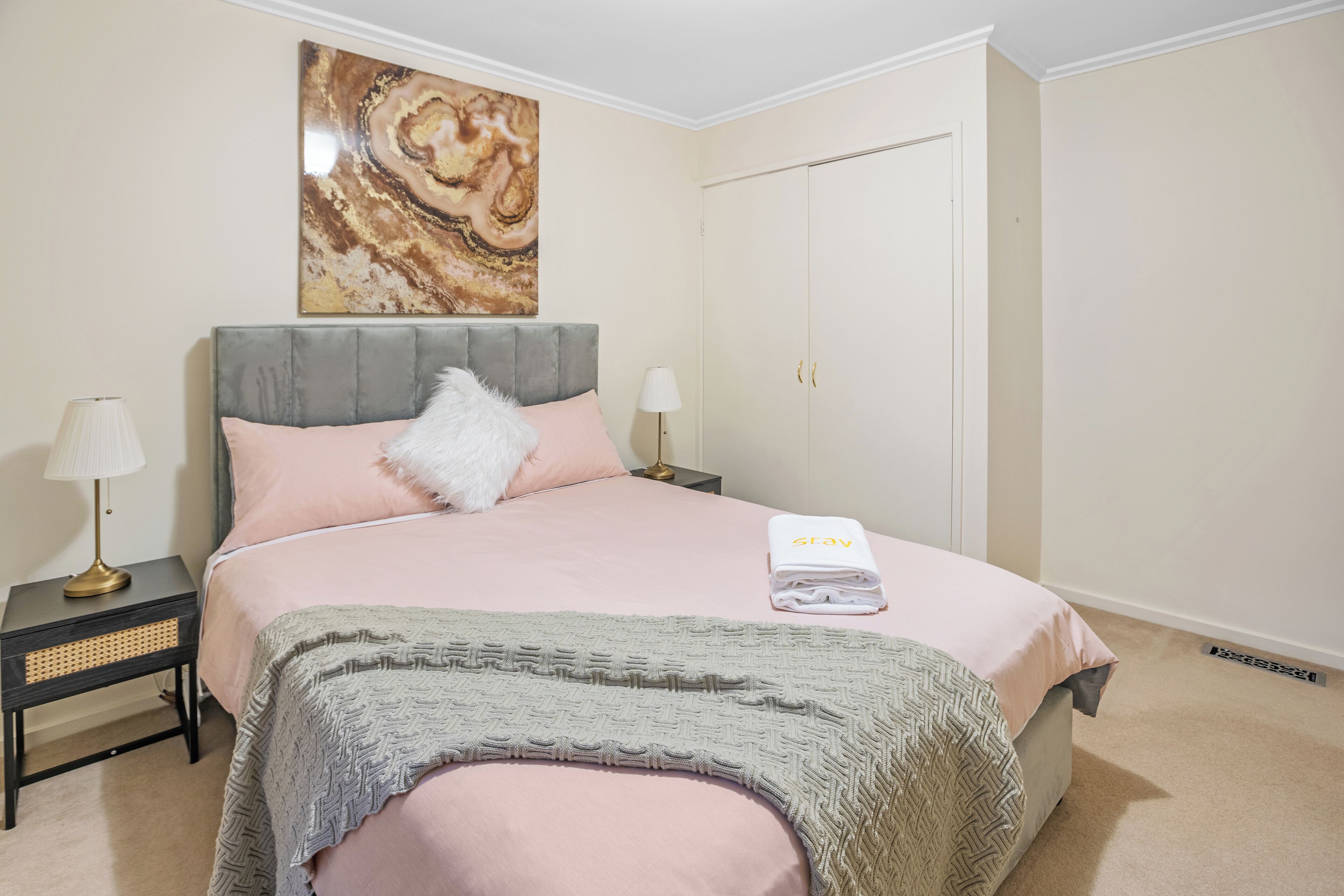 Une chambre bien rangée, avec un lit, une tête de lit, une table de chevet avec une lampe, un tableau décoratif au mur et une porte.