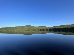 A calm lake reflecting the surrounding forest and hills.