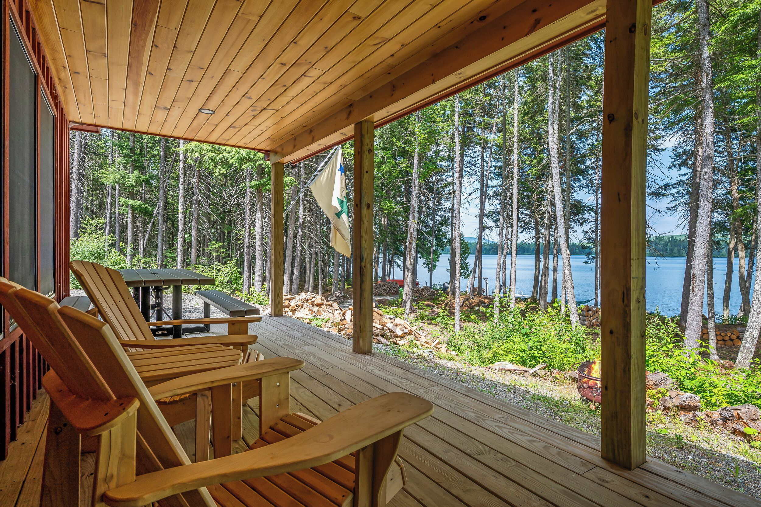 Um deck de madeira com mesa e cadeiras, com vista para um lago cercado por árvores.