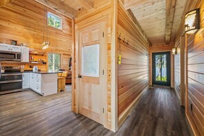 A wooden interior with a kitchen, a dining area, and a hallway leading to a door.