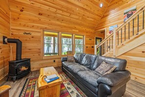 A cozy cabin interior with a fireplace, leather sofa, and a staircase.
