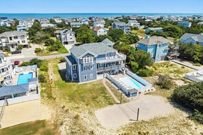 A large house with a swimming pool, surrounded by other houses and a beach.
