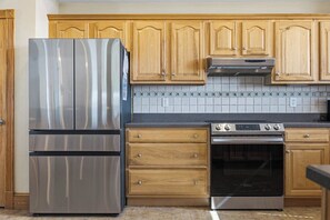 A kitchen with wooden cabinets, a stainless steel refrigerator, a built-in oven, and a tiled backsplash. - Pair-a-dice | 1400 ft to the beach | Private Pool and Hot Tub (Corolla)