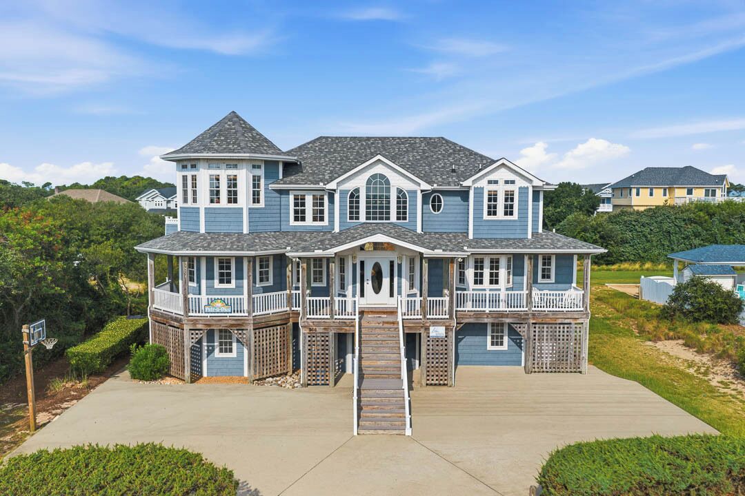 A large, multi-story house with a prominent front porch, multiple balconies, and a driveway leading to the entrance.