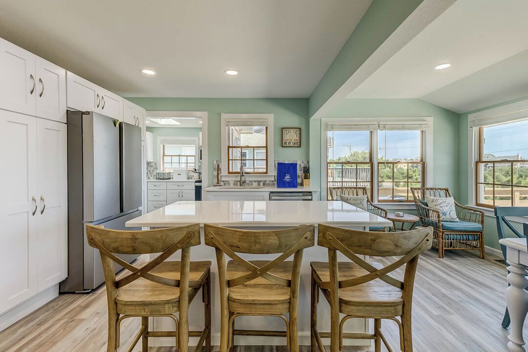 A spacious kitchen with white cabinets, a central island, and wooden chairs.