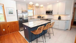 Een moderne keuken met een groot eiland, roestvrijstalen apparatuur en een eethoek met rieten stoelen.